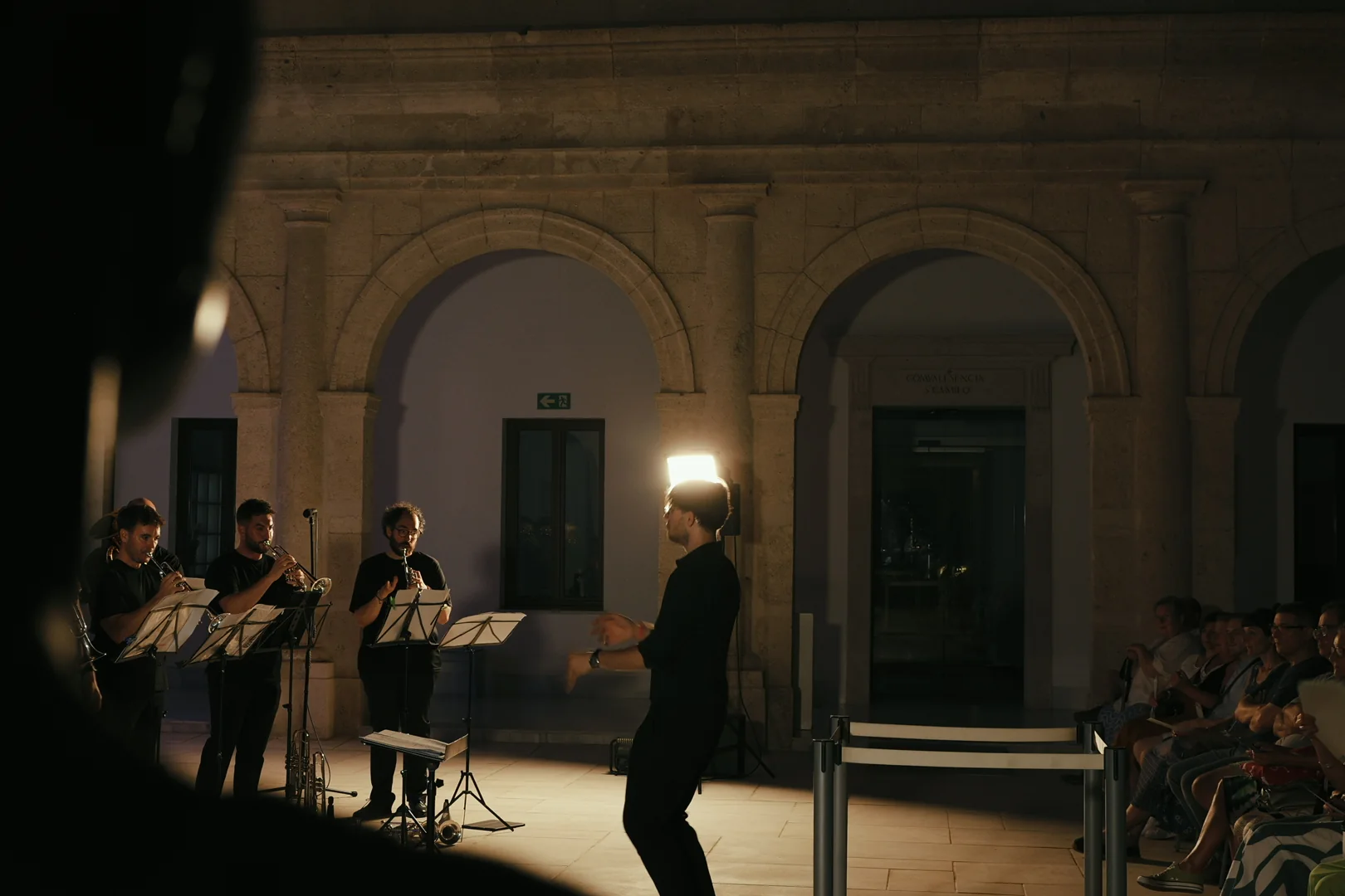Raúl Sabiote dirigiendo un conjunto en un patio con público · Alboran Brass Ensemble · D’Gata Brass Week 2026